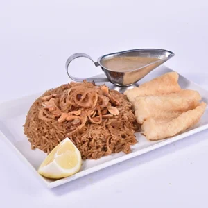 Top-down view of a Middle Eastern vermicelli rice platter with crispy fried chicken strips, a metal gravy boat of tahini sauce, and a lemon wedge on a white rectangular dish.