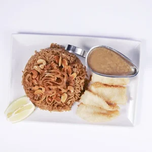 Overhead flat-lay photography of an authentic vermicelli rice and golden fried chicken platter with a metal tahini sauce pitcher and lemon wedge on a white ceramic plate.
