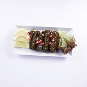 Overhead flat-lay view of an elegant stuffed grape leaves (Dolma) platter, arranged neatly with lemon slices and pomegranate seeds on a white rectangular ceramic plate.