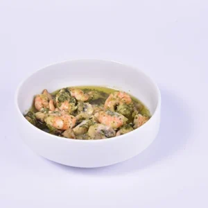 A close-up view of a white ceramic bowl filled with juicy cooked shrimp in a savory garlic and green herb broth, isolated on a clean white background.