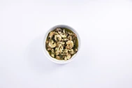 Overhead flat-lay view of a minimalist white bowl filled with sautéed shrimp in a garlic and fresh green herb sauce, set against a plain white surface.