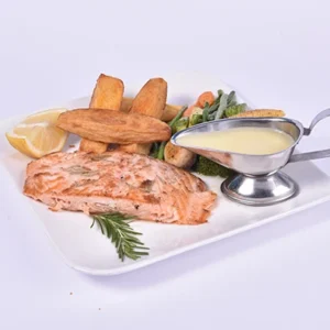 Plated gourmet grilled salmon fillet with crispy potato wedges, mixed seasonal vegetables, a lemon wedge, fresh rosemary, and a silver gravy boat of creamy lemon sauce on a white plate.