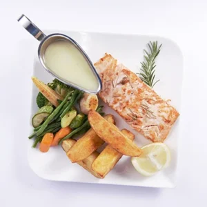 Overhead flat-lay view of a balanced salmon dinner plate with grilled salmon fillet, potato wedges, mixed steamed vegetables, rosemary, lemon, and a metal boat of creamy white sauce.