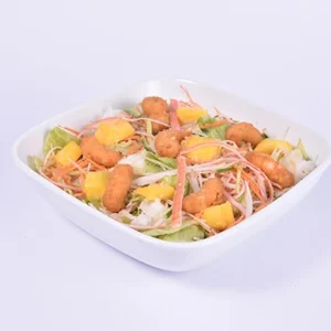 Angled view of a white square bowl filled with a tropical shrimp and pineapple salad, featuring crispy golden shrimp, pineapple chunks, shredded carrots, onions, and lettuce on a white background.