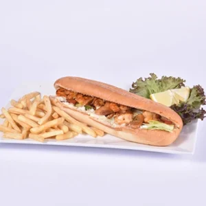Plated crispy shrimp Po' Boy sandwich on a toasted bun with lettuce and creamy sauce, served alongside golden french fries, lemon wedges, and fresh lettuce on a white rectangular plate.