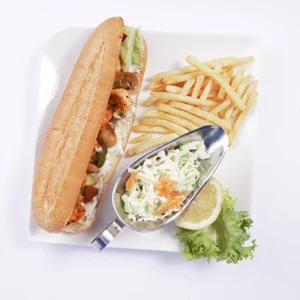 Overhead flat-lay view of a complete seafood sandwich platter featuring a crispy shrimp baguette, golden french fries, a silver bowl of fresh coleslaw, lemon wedges, and red lettuce on a white plate