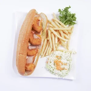 Overhead flat-lay shot of a perfectly plated crispy shrimp hoagie open-faced sandwich, with golden french fries, a round bowl of creamy coleslaw, lettuce, and lemon on a white square plate.