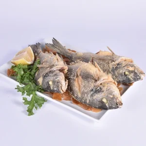 Plated whole grilled fish served on a white rectangular plate, garnished with fresh lemon slices and crisp curly lettuce against a clean white background.
