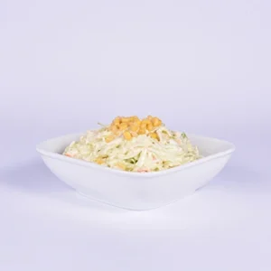 Eye-level shot of a fresh creamy coleslaw salad served in a white square bowl, topped with sweet yellow corn kernels, with a clean white background.