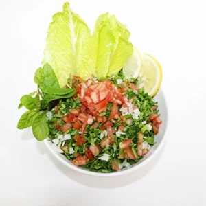 A fresh traditional Lebanese tabbouleh salad served in a white bowl, featuring finely chopped parsley, tomatoes, mint leaves, and lemon slices with crispy lettuce cups.