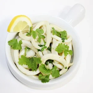 A white bowl with a handle filled with white calamari rings topped with fresh green parsley and a lemon wedge on a clean white background.
