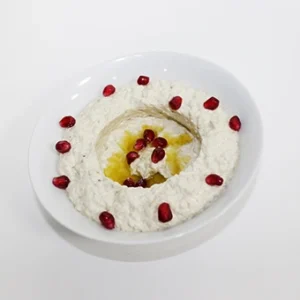 A white bowl of creamy smoked eggplant dip, garnished with pomegranate seeds and a swirl of olive oil, on a clean white background.
