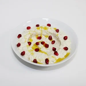 A white bowl of creamy smoked eggplant dip, garnished with a ring of pomegranate seeds and a swirl of olive oil, on a clean white background.