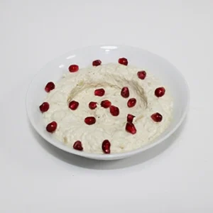 A white bowl of creamy smoked eggplant dip, garnished with a ring of pomegranate seeds and a swirl of olive oil, on a clean white background.