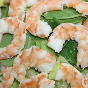 A close-up view of a fresh salad featuring cooked shrimp, fresh spinach leaves, and green avocado slices.