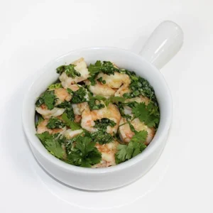 Top view of a white bowl filled with sauteed shrimp tossed in garlic, lemon, and fresh parsley on a clean white background.