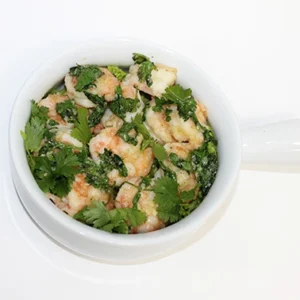 A white bowl with a handle filled with shrimp tossed in garlic, lemon, and fresh parsley, shown from a top view.