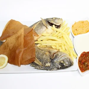 A white plate featuring a whole grilled fish, golden fries, crispy flatbread, lemon slices, and a side dish with three dipping sauces.
