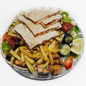 Close-up of grilled chicken chunks with crispy fries, grilled vegetables, and layered flatbread topped with sauce, served with lemon on a foil plate.