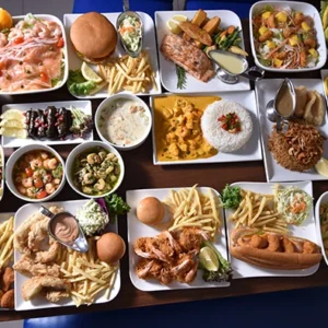 A top view of a grand family feast platter with fried shrimp, crispy chicken, salads, fried rice, french fries, and dipping sauces on a square white table.