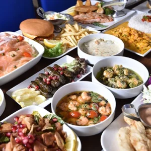 A top-view of a large family feast platter filled with grilled meats, seafood, soups, salads, and assorted side dishes on a large table.