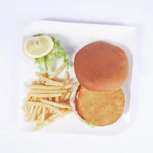 A crispy golden chicken fillet sandwich in a soft bun served with french fries and a lemon wedge on a white plate.