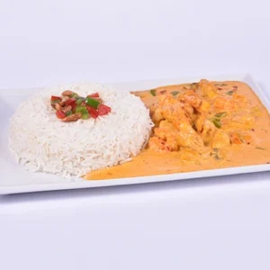 A white rectangular plate featuring a mound of steamed white rice garnished with diced tomatoes and peppers, served with a creamy orange chicken curry sauce on the side.