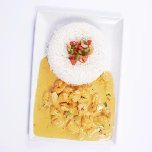 A white rectangular plate featuring a mound of steamed white rice garnished with red and green peppers, served with a rich, creamy yellow chicken curry sauce.