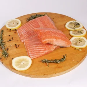 Fresh salmon fillets on a wooden cutting board, surrounded by fresh lemon slices, sprigs of rosemary, and peppercorns.