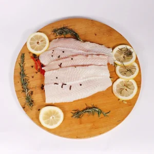 Fresh white fish fillets with lemon slices, rosemary, and peppercorns arranged on a wooden cutting board.