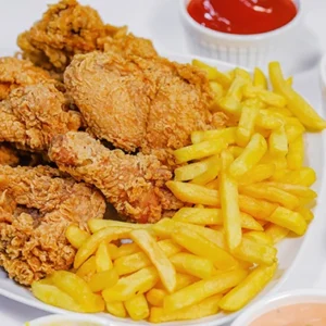 A white platter filled with golden crispy fried chicken pieces and a large pile of golden french fries, accompanied by small bowls of dipping sauces.