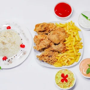 A wide top-down view of a white table featuring a central platter of golden crispy fried chicken or seafood, surrounded by plates of fluffy spiced rice, french fries, creamy coleslaw, and five small bowls of colorful dipping sauces garnished with fresh mint leaves.