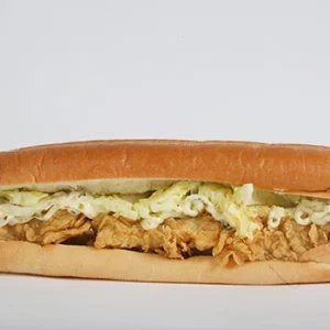 A close-up of a long French roll sandwich filled with golden crispy chicken strips, fresh shredded lettuce, and creamy white mayo sauce .