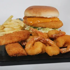 A black serving board featuring a crispy fish fillet sandwich with melted cheddar cheese, surrounded by golden fried whole shrimp, crunchy fish fingers, french fries, and a small bowl of creamy white sauce.