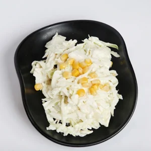 A top-down view of a black wavy bowl filled with freshly shredded white cabbage and scattered sweet yellow corn kernels on a plain white background.