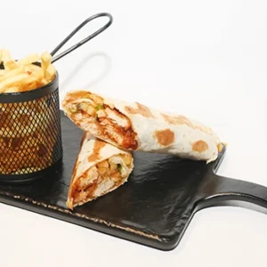 A black serving board with a toasted tortilla wrap cut into two halves showing a cheesy filling, placed next to a black metal basket filled with golden crispy french fries.