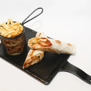 A black serving board featuring a grilled wrap cut into two halves showcasing its filling, accompanied by a small black metal basket filled with golden crispy french fries.